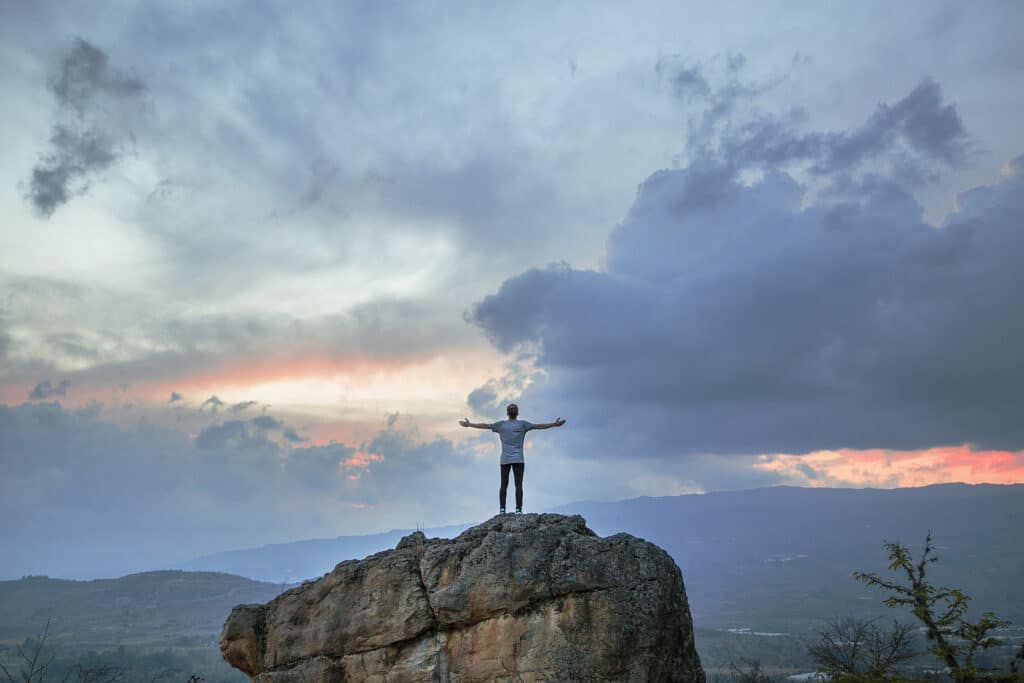 Person standing on top of a mountain, symbolizing the achievement of financial freedom through alternative savings methods