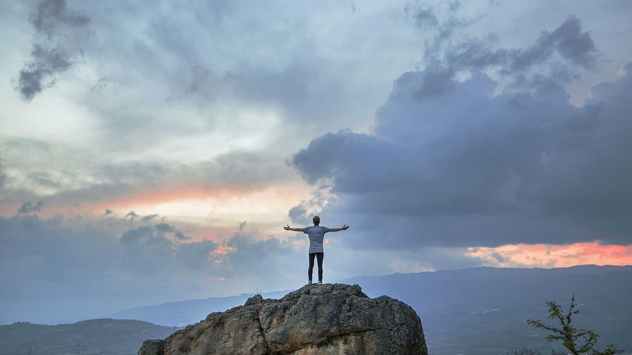 Person standing on top of a mountain, symbolizing the achievement of financial freedom through alternative savings methods