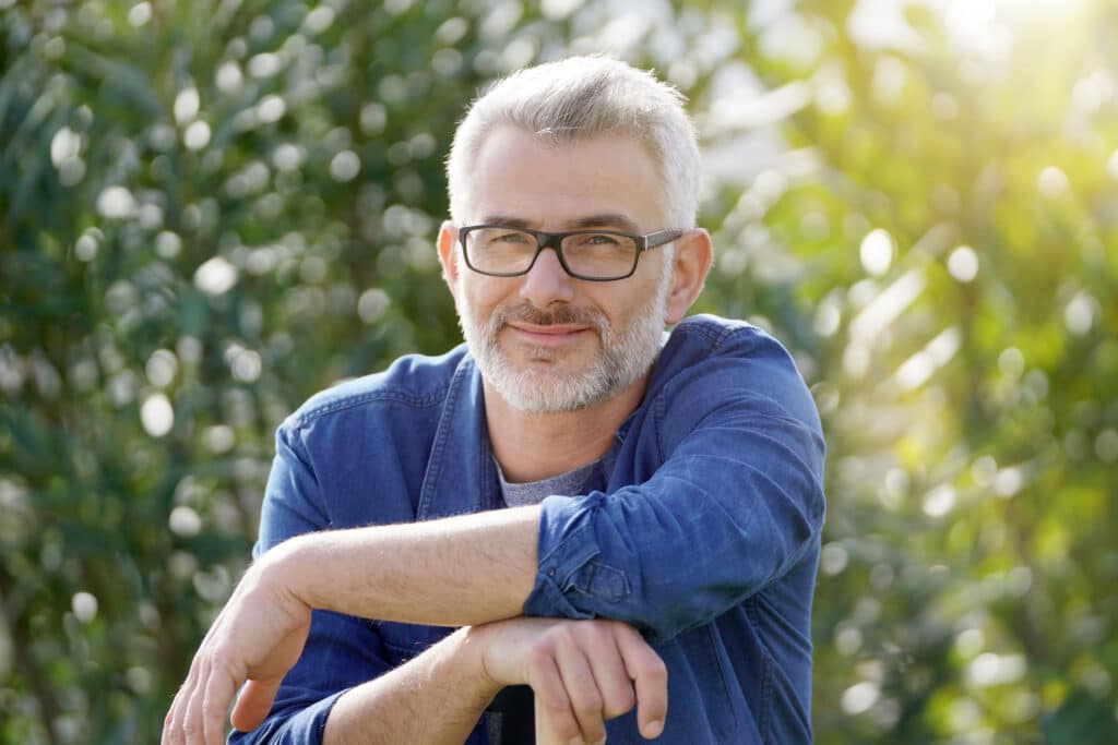 Smiling, contemplative man in his fifties wearing a blue plaid flannel, thinking about his debt-free future on a sunny day outdoors.