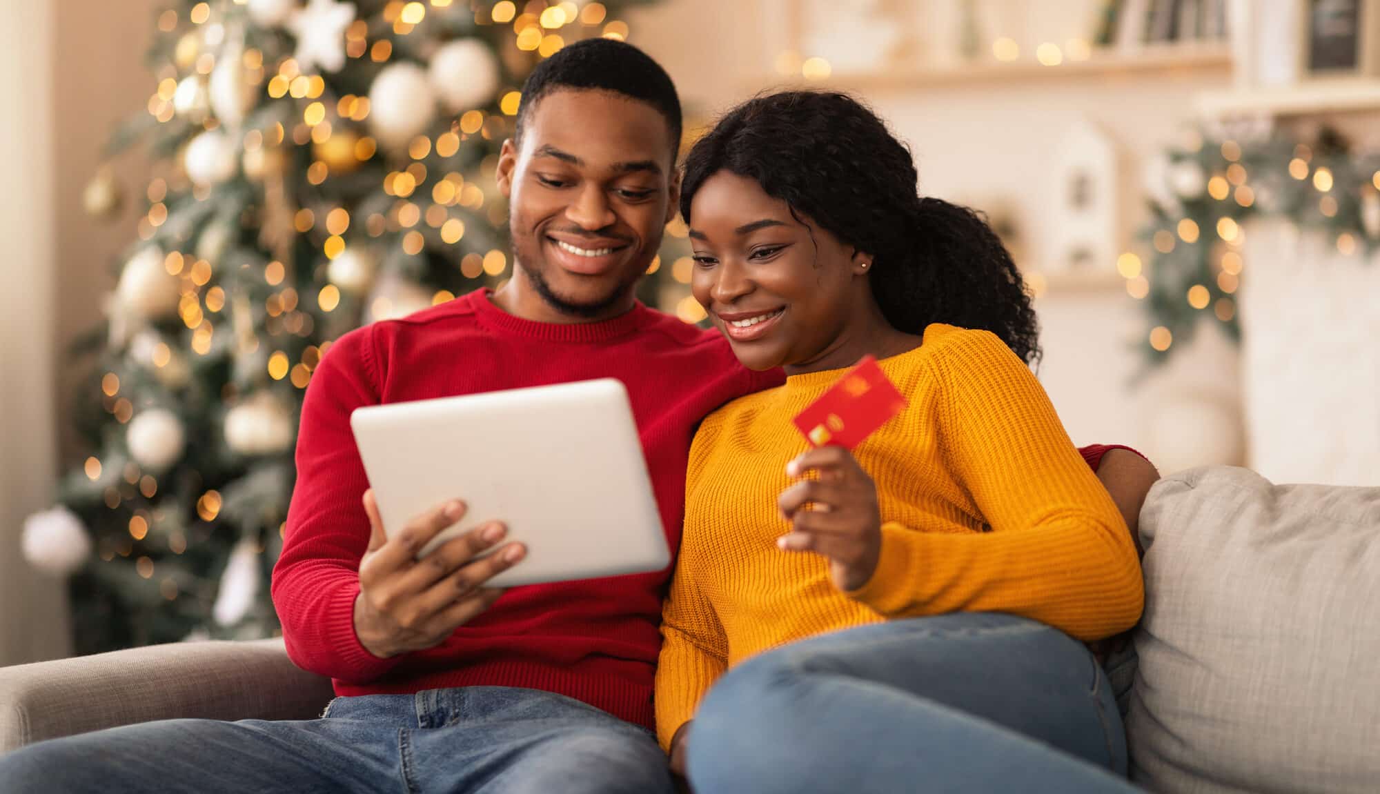 Couple reviewing online purchases on a tablet while holding a credit card during the holiday season
