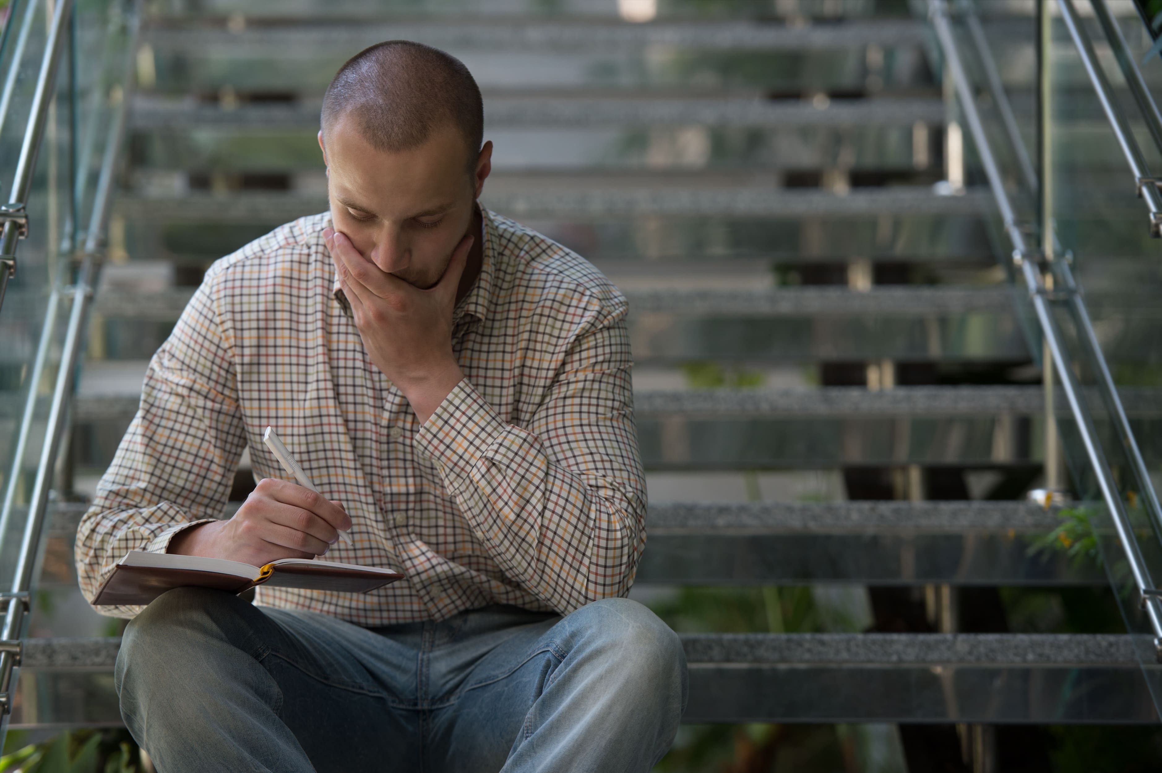 A man sitting on steps, writing on a pad of paper and looking determined.