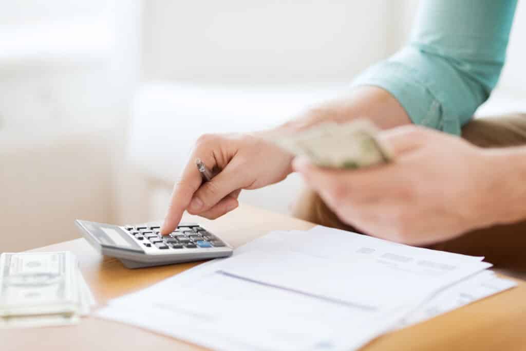 A person using a calculator to budget their finances, with papers and cash on the desk.