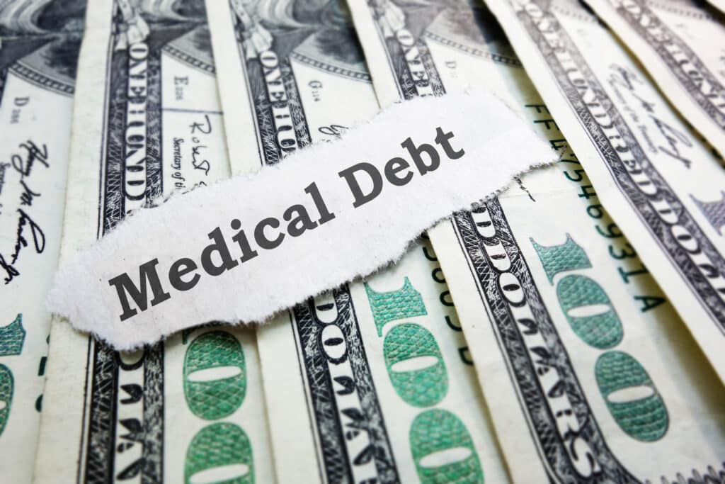 The words medical debt on top of 100 dollar bills.