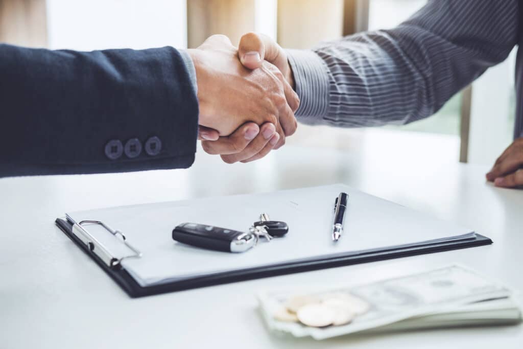 Handshake between auto salesman and customer above a contract with keys on it.