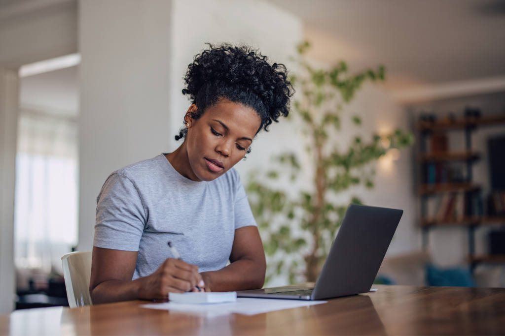 Woman reviewing her finances with a notebook and laptop at home