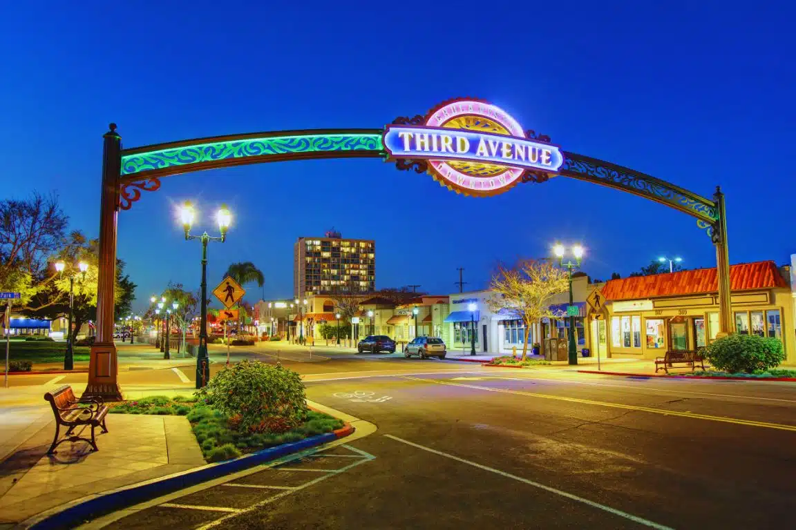 Chula Vista gateway arch lit at night with shops, streetlights, and downtown buildings in the background.