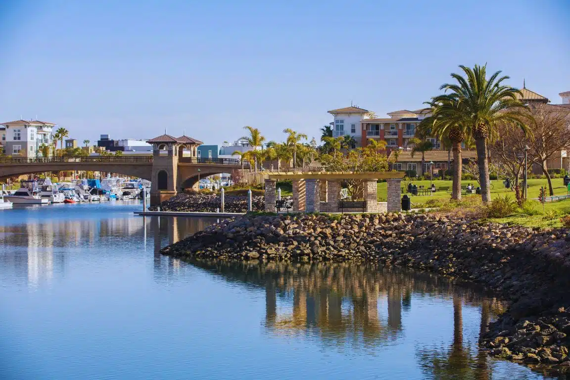 Channel Islands Harbor in Oxnard with boats, waterfront homes, palm trees, and a pedestrian bridge.