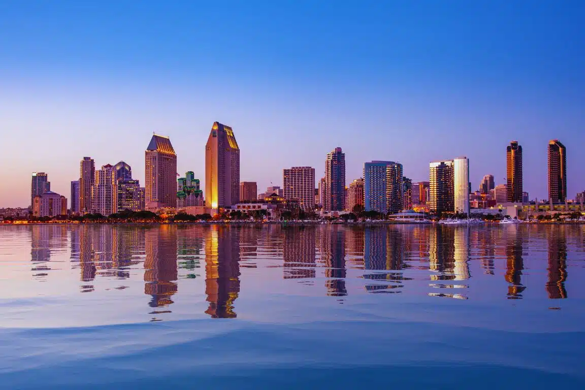 San Diego skyline at dusk with high-rise buildings reflected across the calm waters of the bay.