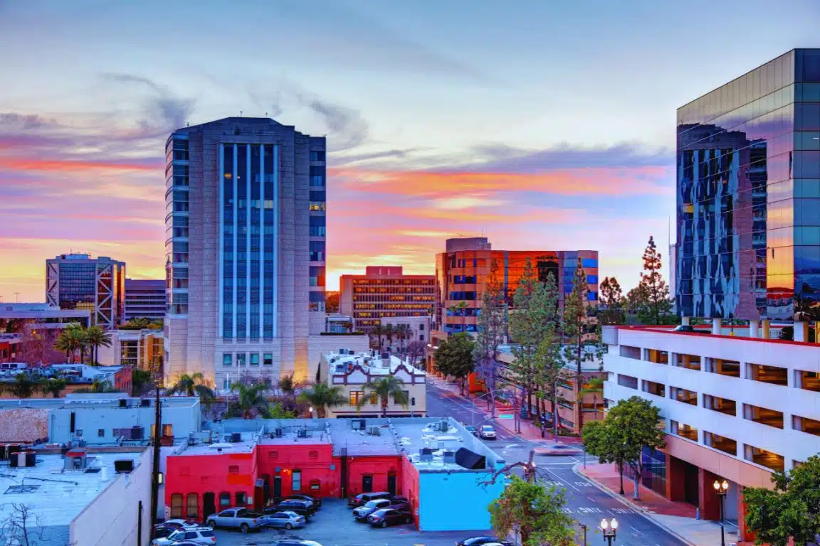 Downtown Santa Ana skyline at sunset with office towers, colorful low-rise buildings, and a vivid evening sky.