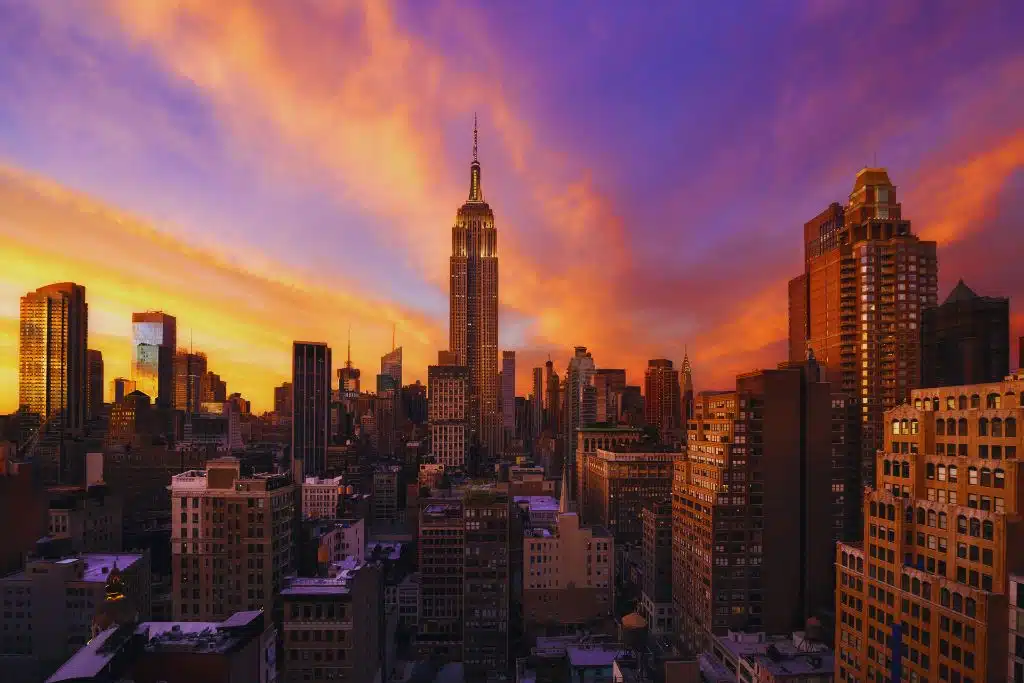 Manhattan skyline at sunset with the Empire State Building centered beneath vivid orange and purple clouds.
