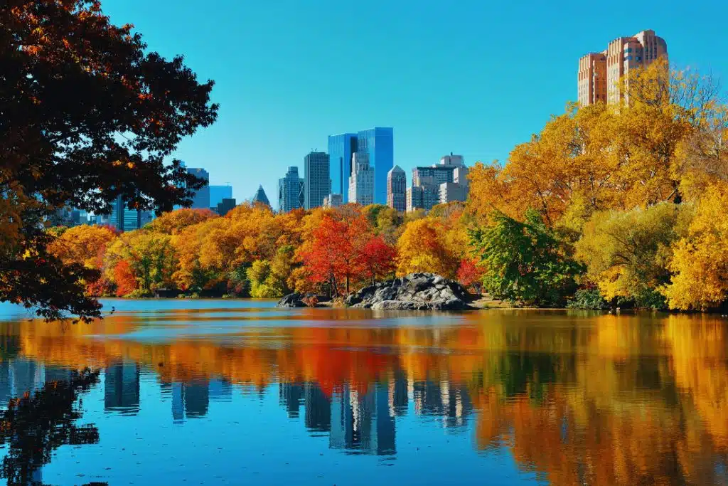 Iconic New York City skyline at dusk with illuminated skyscrapers, bridges, and the Hudson River reflecting city lights.