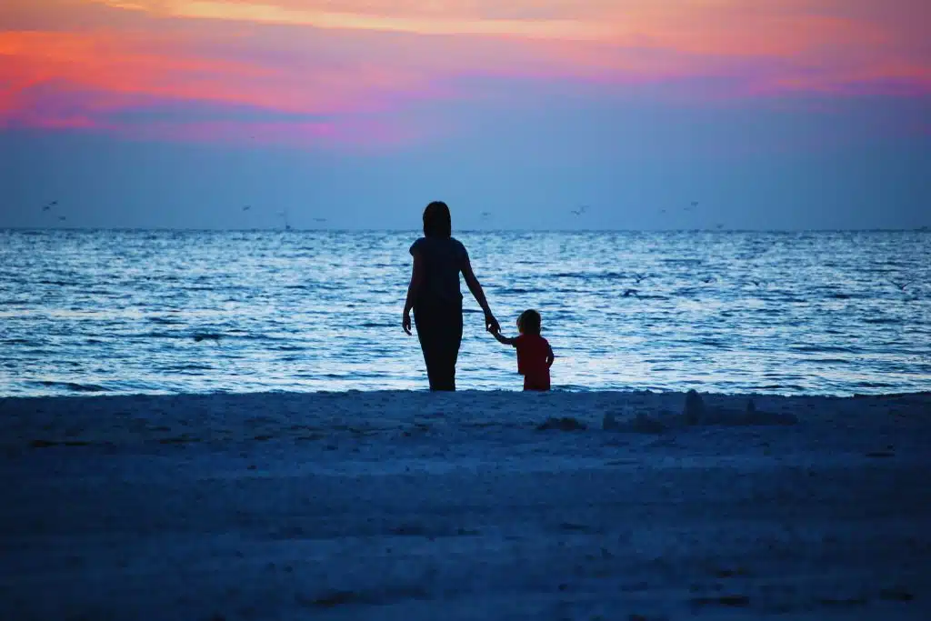 Serene Oyster Bay harbor with sailboats docked, historic homes along the shore, and calm water reflecting a clear sky.