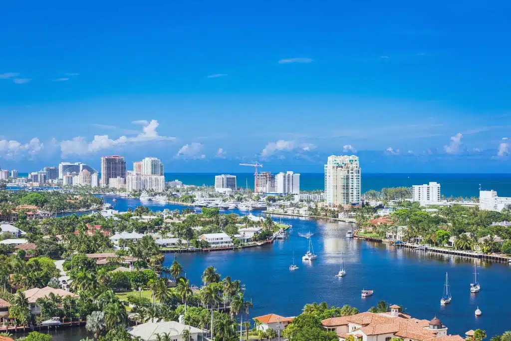 Fort Lauderdale beachfront with palm trees, turquoise water, and skyline of high-rises at golden hour.