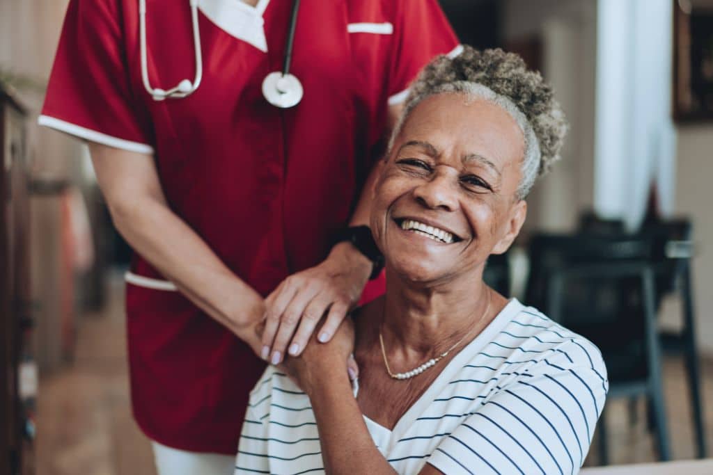 Care professional standing beside an older woman in a calm, supportive setting