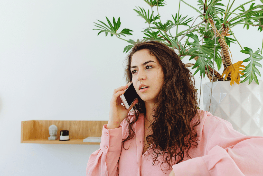 Woman in a pink top talking on a phone in a kitchen.