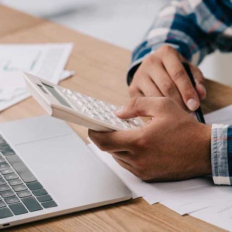 Budgeting Calculations Person using a calculator at a desk with a laptop and papers, possibly managing finances or doing taxes.